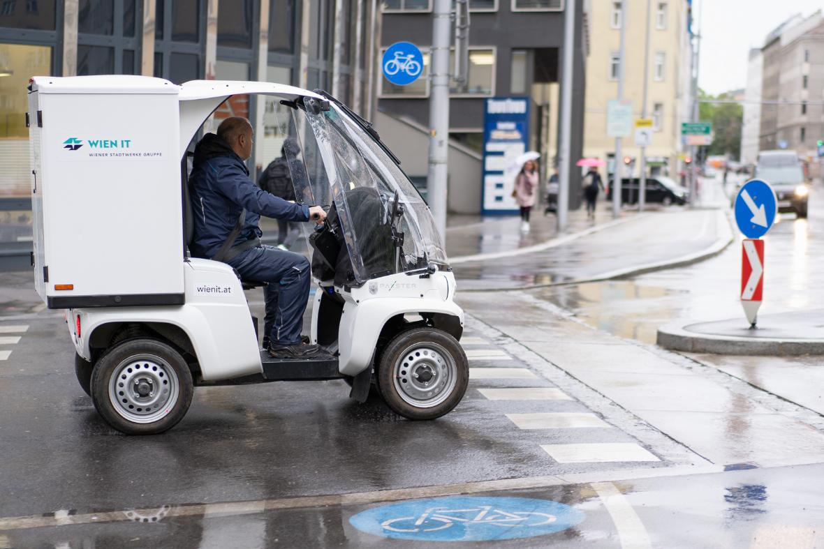 Ein weißes Auslieferungs-Fahrzeug auf der Straße mit Windschutzscheibe, seitlich fotografiert. Ein Fahrer sitzt drinnen.